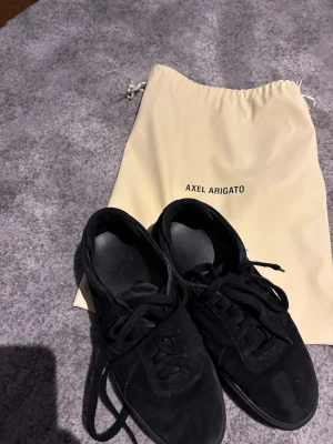 Svarta sneakers från Axel Arigato - Snygga helsvarta sneakers från Axel Arigato i mocka med klassisk låg profil och svarta skosnören. Skorna har en stilren design och kommer med original dustbag. Perfekta för dig som gillar minimalistisk och clean stil. Samt riktigt bra pris då dom e knappt använda och nypris 2800
