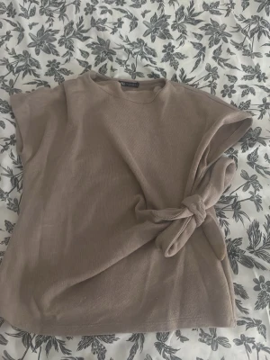 Beige ribbad topp med knyt - Säljer en beige ribbad topp från Vila med korta ärmar och snygg knytning i sidan. Toppen har en rund halsringning och är gjord i ett mjukt material som känns skönt mot huden. Perfekt att styla med jeans eller kjol.
