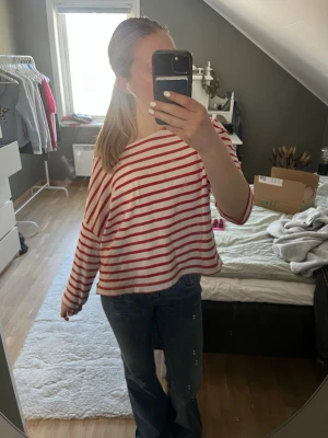 Randig rödvit långärmad topp - Säljer en loose fit topp med röda och vita ränder. Toppen har långa ärmar och en avslappnad passform med bred halsringning. Perfekt för en chill och enkel stil. Materialet känns mjukt och skönt, troligtvis bomull.