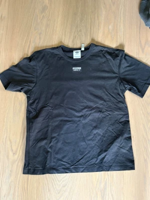 Svart Adidas t-shirt med logga - Snygg svart t-shirt från Adidas med liten broderad logga på bröstet. Klassisk rund halsringning och korta ärmar. Tillverkad i mjuk bomull som känns skön mot huden. Perfekt till jeans eller shorts för en clean och sportig look.