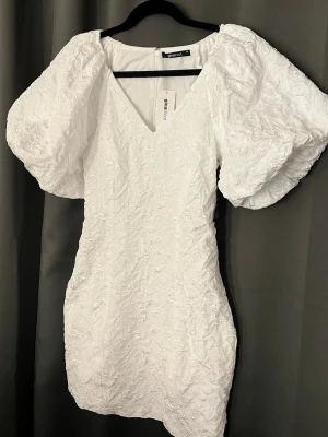 Vit Studentklänning från Gina Tricot  - Vacker vit studentklänning från Gina Tricot med puffiga korta ärmar och v-ringning. Klänningen är figursydd, se bilder för material på tyget. Klänningen är oanvänd med prislappen kvar. Säljer då jag köpte två andra💗 