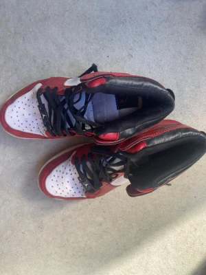 Rödvita Nike high-top sneakers - Snygga high-top sneakers från Nike i rött och vitt med svarta skosnören och svart vadderad insida. Klassisk design med perforerad tå och vit sula. Perfekta för dig som gillar streetstyle och vill sticka ut med en ikonisk look.