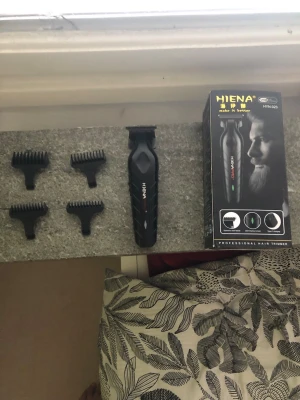 Hiena svart hårtrimmer med tillbehör - Säljer en svart hårtrimmer från Hiena, .Medföljer fyra svarta kammar i olika längder för flexibel styling. Trimmern har ergonomiskt grepp och modern design. Perfekt för att fixa håret eller skägget hemma. Guards kommer med den samma guards som clippern