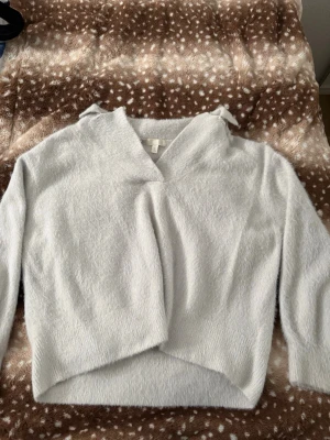 Ljusgrå fluffig omlottkofta H&M - Mysig ljusgrå omlottkofta från H&M i fluffigt material. Koftan har en avslappnad passform, V-ringning och långa ärmar. Perfekt för lager på lager och ger en trendig look till din outfit.