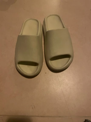 Beige chunky tofflor i skum - Säljer ett par beige chunky tofflor med öppen tå och bred rem. Tillverkade i mjukt och flexibelt skummaterial för extra komfort. Perfekta att glida i hemma eller till och från gymmet. Snygg minimalistisk design som passar till det mesta.