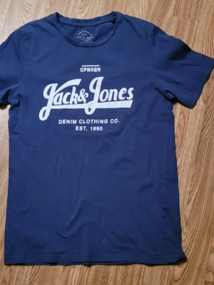 Blå Jack & Jones t-shirt med tryck - Snygg marinblå t-shirt från Jack & Jones med vitt tryck framtill. Klassisk passform och rund halsringning. Tillverkad i mjuk bomull som känns skön mot huden. Perfekt för en avslappnad och stilren look.