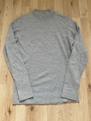 Grå stickad tröja från Lindbergh - Snygg grå stickad tröja från Lindbergh med högre rundad hals och långa ärmar. Tröjan har en enkel och stilren design som passar perfekt till olika outfits. Materialet känns mjukt och bekvämt mot huden.