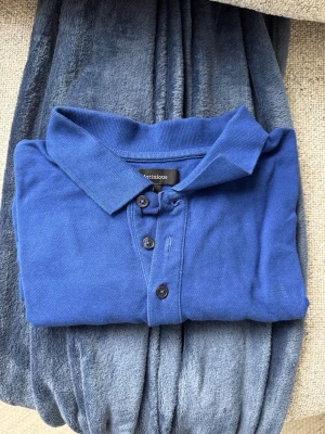 Blå pikétröja från Matinique - Klassisk blå pikétröja från Matinique med krage och tre knappar framtill. Tillverkad i mjuk bomull och har korta ärmar. Perfekt för en avslappnad men ändå stilren look.