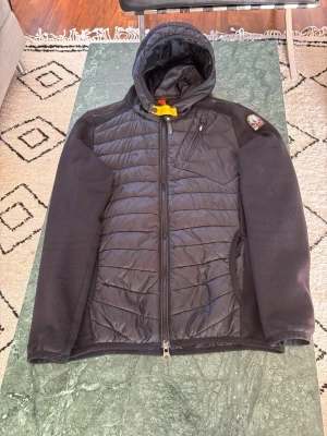 PARAJUMPER CARDIGAN  - Svart vindjacka från Parajumpers med huva och dragkedja framtill. Jackan har quiltade partier på bröst och rygg, mjuka ärmar och en gul detalj vid halsen. Märkespatch på vänster ärm och praktiska fickor med dragkedja. Perfekt för dig som vill ha en stilren och funktionell jacka. Äkta givetsvis, inga skador eller hål,  kom dm för fler bilder eller evenutellla frågor:)