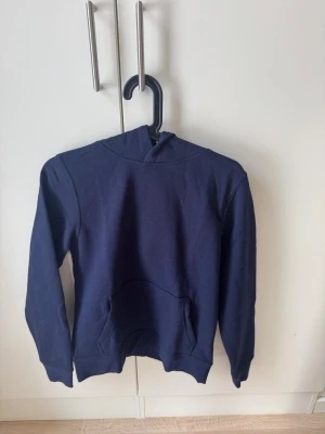 Mörkblå hoodie med magficka - En enkel och stilren mörkblå hoodie med huva och stor magficka framtill. Hoodien har långa ärmar och ribbade muddar vid ärmslut och nederkant. Perfekt för en avslappnad look och passar till det mesta. Materialet känns mjukt och bekvämt, troligen bomull eller bomullsblandning. Helt ny och aldrig använd, köpt för 500 och säljer för halva priset. Pris kan diskuteras💕💕