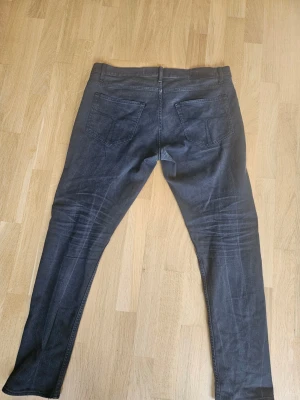 Svarta Tiger of Sweden slim fit jeans - Säljer ett par svarta slim fit jeans med klassisk femficksdesign och snygga slitningar på framsidan. Jeansen har normal midja och smala ben. Perfekta för dig som gillar en modern och stilren look.