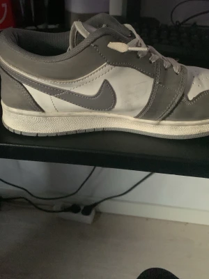 Nike Dunk Low gråvita sneakers - Nike Dunk Low sneakers i grått och vitt med klassisk Swoosh-logga på sidan. Ovandelen är i läder med perforerad tåbox och vita skosnören. Snygg retrostil som passar till många outfits.