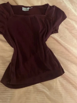 Vinröd topp  - Snygg vinröd topp med korta ärmar och fyrkantig ringning. Figurnära passform och mjukt material som känns skönt mot huden. Perfekt att styla med jeans eller kjol för en trendig look.