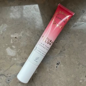 Lumene Natural Glow Coral Blush - Flytande rouge från Lumene i nyansen Coral Blush. Tuben har en snygg ombre-design i rosa och vitt med guldtext. Produkten är vegansk och innehåller 20 ml. Perfekt för att ge kinderna en naturlig, fräsch lyster.