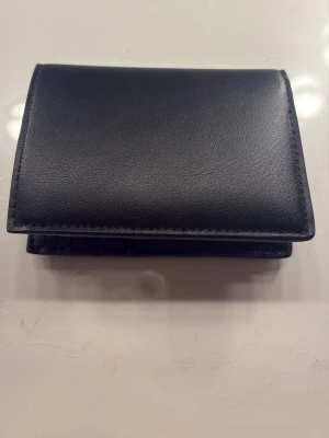 Svart stilren läderplånbok - Säljer en svart plånbok i slätt läder med enkel och stilren design. Plånboken har flera kortfack på insidan och är perfekt för dig som vill ha en smidig och klassisk accessoar. Passar lika bra i fickan som i väskan.