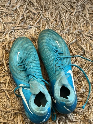 Nike Phantom gx blå fotbollsskor - Säljer ett par blå Nike Phantom fotbollsskor med vita detaljer och snörning. Väldigt sköna skor men som man ser är dom välanvända. Det ända problemet dock är sulan på ena skon är sönder. Nypris 2799kr