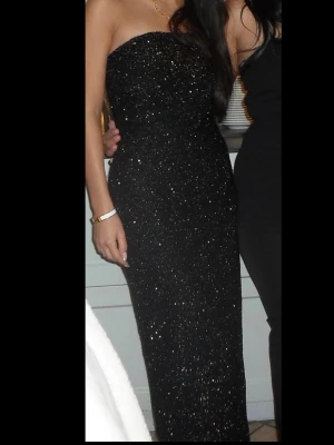Svart glittrig axelbandslös långklänning - Säljer en svart, glittrig långklänning med axelbandslös design. Klänningen har en figurnära passform och är täckt av små glittrande detaljer som ger en lyxig känsla. Perfekt för dig som vill sticka ut på bal eller fest. Endast använd en gång 🖤