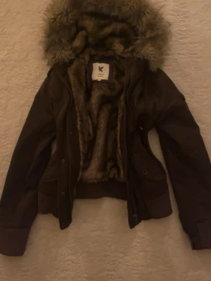 Jättefin brun jacka med fuskpäls - Mysig brun pufferjacka från Surplus raw vintage med fluffigt foder och stor huva med fuskpäls (fuskpälsen på huvan går att ta av). Jackan har ribbade muddar, fickor med lock och dragkedja samt knappar framtill. Perfekt för kalla vinterdagar och riktigt varm! Jag har skrivit märket som Abercrombie för det ska nå ut, men notera att det inte är det riktiga märket. Storleken är M men jag skulle säga att det passar S-XS bättre :) 