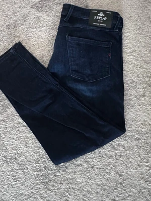 Mörkblå slim jeans från Replay - Snygga mörkblå slim fit jeans från Replay med klassisk femficksdesign och diskret logga på fickan. Jeansen har raka ben och är tillverkade i mjukt denimtyg som ger en skön passform. Perfekta för dig som gillar stilrena och tidlösa jeans. W 34 L 30 