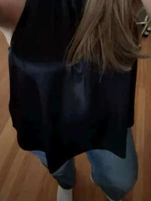 Svart satin topp - Snygg svart linnetopp i glansigt satinmaterial. Toppen är ärmlös med hög halsringning och har en lös passform. Perfekt inför sommaren. Skicka gärna frågor och prisförslag 