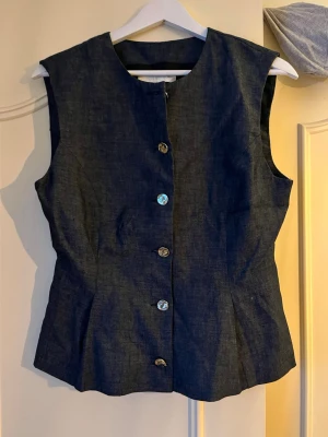 Mörkblå topp med knappar - Snygg mörkblå ärmlös topp från Zara med rund halsringning och silverfärgade knappar framtill. Toppen har figurnära passform. Helt ny med lappen kvar, då jag inte hann lämna tillbaka för den satt inte som jag ville. Pris kan diskuteras