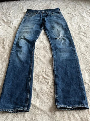 Levi's blå raka jeans herr - Klassiska blå jeans från Levi's med rak passform och slitningar på knäna. Jeansen har fem fickor, knappgylf och den ikoniska röda Levi's-lappen bak. Tillverkade i slitstark denim med snygg tvätt och detaljerade sömmar. Perfekt för archive stil pga den vintage patina slitning med honeycombs osv. W 28 L32     Meddela för mått i cm