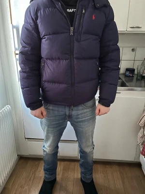 Mörkblå pufferjacka från Ralph Lauren - Snygg mörklila pufferjacka från Ralph Lauren med dragkedja framtill och två sidofickor med dragkedja. Jackan har hög krage och den klassiska röda loggan broderad på bröstet. Perfekt för kalla dagar och ger en riktigt modern look. Pris går att diskuteras 