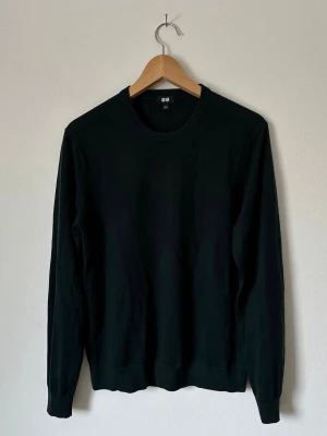 Mörkgrön stickad tröja från Uniqlo - En stilren mörkgrön stickad tröja från Uniqlo med rund halsringning och långa ärmar. Tröjan har ribbade muddar vid ärmslut och nederkant. Perfekt basplagg för lager på lager och enkel att matcha med olika outfits. 8A16