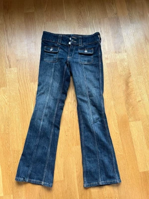 Mörkblå bootcut jeans - Snygga mörkblå bootcut jeans med dubbla knappar i midjan och två framfickor med lock och knappdetaljer. Storlek 140