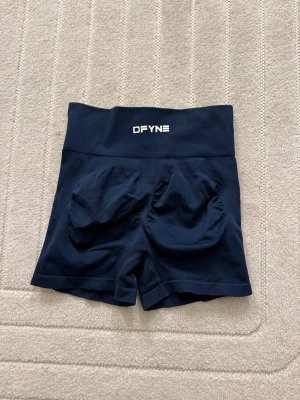 Mörkblå träningstights-shorts från DFYNE - Säljer ett par mörkblå,  träningstights-shorts från DFYNE. De har en bred resår i midjan och sömlös design för extra komfort. Perfekta för gymmet eller löprundan. Materialet är stretchigt och andas bra.