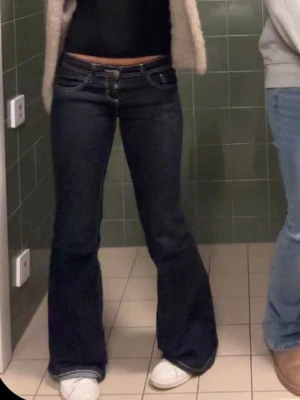 Mörkblå bootcut jeans med låg midja - Säljer ett par mörkblå bootcut jeans med låg midja och klassiska fem fickor. Jeansen har kontrastsömmar och utsvängda ben, perfekta för en trendig och avslappnad look. Materialet är denim med lite stretch för extra komfort.