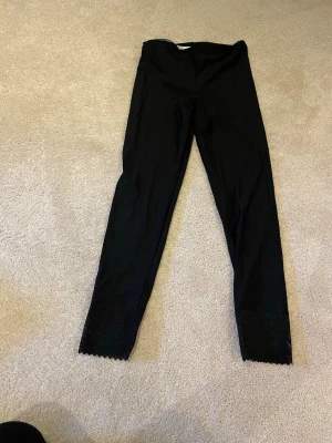 Svarta leggings med spetskant - Säljer ett par svarta leggings från Miss Mary med snygg spetskant längst ner vid bensluten. De är stretchiga och har en hög midja, perfekta till en oversized tröja eller hoodie. Materialet känns mjukt och bekvämt mot huden.