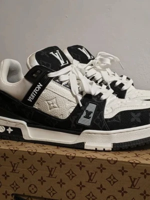 Louis Vuitton svartvita sneakers - Säljer ett par Louis Vuitton sneakers i svart och vitt med klassiskt LV-monogram på både ovandel och plös. Skorna har vita snören, robust sula och detaljer i läder och textil. Perfekta för dig som vill sticka ut med exklusiv design och streetwear-vibe.