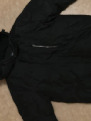 Svart pufferjacka - Säljer en svart pufferjacka från Take Off med hög krage och dragkedja framtill. Jackan har en slät yta och en bröstficka med dragkedja. Perfekt för kalla dagar och riktigt skön att bära.