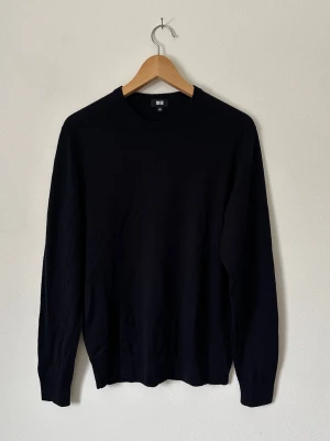 Mörkblå stickad tröja från Uniqlo - En stilren mörkblå stickad tröja från Uniqlo med rund halsringning och långa ärmar. Tröjan har en enkel och klassisk design som passar till det mesta. Perfekt för lager på lager och funkar året runt. 8C27