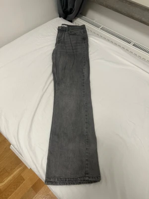 Grå raka jeans med hög midja - Säljer ett par grå jeans med rak passform och hög midja. Jeansen har klassisk femficksdesign och stängs med knapp och dragkedja. Materialet är denim i bomull och färgen är en snygg tvättad grå. Perfekta till en avslappnad stil.