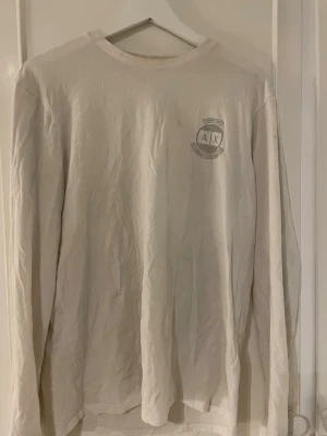 Vit långärmad topp från Armani Exchange - Vit långärmad topp från Armani Exchange med rund halsringning och diskret logga på bröstet. Tillverkad i mjuk bomull, perfekt för en clean och enkel stil. Passar till det mesta och är lätt att matcha.
