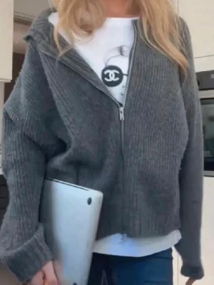 Grå stickad zip-kofta - Mysig grå stickad kofta med dragkedja framtill. Koftan har en avslappnad passform, långa ärmar och en hög krage. Perfekt att slänga på sig över en t-shirt för en chill look.