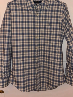 Rutig Ralph Lauren skjorta - En rutig Ralph Lauren skjorta i hög kvalitet. Den är blå och beige/vit. Använd max 2 gånger så den är i nyskick. Säljer då den är för liten för mig. Tveka inte på att skriva vid funderingar!😀  (Äkthets tag tillkommer)