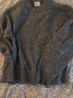 Grå stickad tröja med glitterdetaljer - Mysig grå stickad tröja med glittriga detaljer som ger en extra touch. Tröjan har rund halsringning, långa ärmar och ribbade muddar. Kan även passa dig som vanligtvis bär S. Tror att jag köpte den för runt 150/200 kr ny och är bara använd en gång, därför lägger jag priset ganska högt men det kan även diskuteras.