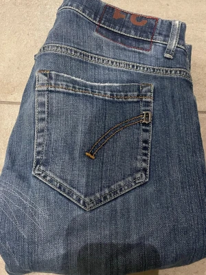 Blå jeans från dondup med raka ben - Snygga blå jeans från dondup klassisk femficksdesign och raka ben. Jeansen har en cool detalj på bakfickan med kontrastsöm och metallspänne. Tillverkade i slitstark denim med lätt tvättad look och diskreta slitningar. Jeans har en  defekt vid rumpan som ej syns vid användning 