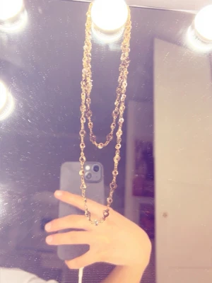 Guldigt halsband.  - Säljer ett långt, dubbelt halsband i guldfärgad metall med små pärlor infällda längs hela kedjan. Halsbandet har en elegant och trendig look som passar perfekt till olika stilar.  Gå in på mitt konto jag säljer FLERA smycken i olika former och färger. 😊