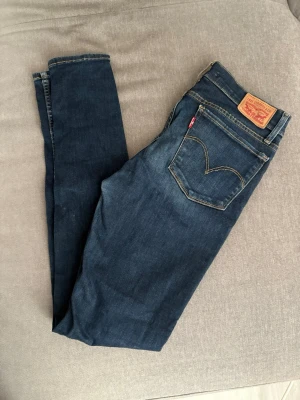 Mörkblå Levi's jeans superskinny 29/32 - Snygga mörkblå superskinny jeans från Levi's med klassisk rak passform och femficksmodell. Jeansen har kontrastsömmar, läderpatch bak i midjan och den ikoniska röda Levi's-taggen på bakfickan. Tillverkade i slitstark denim, perfekta för en avslappnad stil.