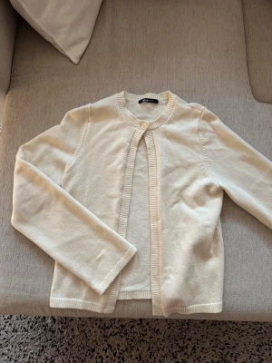 Vit kofta från Gina Tricot - Klassisk vit kofta från Gina Tricot med rund halsringning och ribbade kanter. Koftan har en enkel knapp framtill och är tillverkad i mjukt stickat material. Perfekt att slänga över en topp för en clean look.