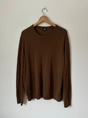 Brun stickad tröja från Uniqlo - En enkel och stilren brun stickad tröja från Uniqlo. Tröjan har rund halsringning, långa ärmar och ribbade muddar vid ärmslut och nederkant. Perfekt för lager på lager och passar till det mesta i garderoben. 8C17