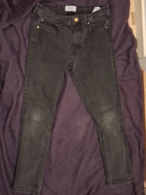 Svarta skinny jeans från Slease - Säljer ett par svarta skinny jeans från Slease by Stock & Hank. Jeansen har klassisk femficksmodell, guldfärgade nitar och knapp, samt dragkedjegylf. Materialet är stretchigt för en bekväm passform.