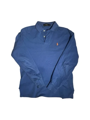 Ralph Lauren långärmad pikétröja - Säljer en snygg blå långärmad pikétröja, och befinner sig i mycket bra skick med inga defekter! Skriv om fler bilder behövs, skickar så snabbt jag kan! 🙌🏼  🤏🏼 | Storlek: XS 🎨 | Färg: Blå & Orange <> | Bredd: 47cm  ↑↓| Längd : 67cm