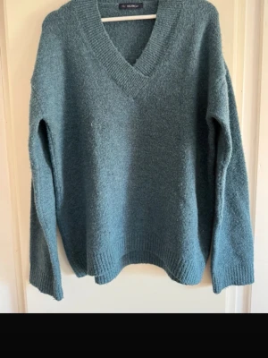 Blå stickad tröja från Dilvin - Mysig blå stickad tröja från Dilvin med v-ringad hals och ribbade muddar vid ärmslut och nederkant. Tröjan har en avslappnad passform och är perfekt för kyliga dagar. 