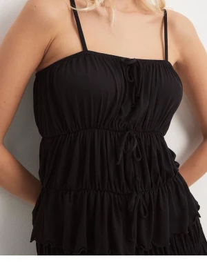Svart topp med smala band - Svart topp med smala axelband och flera snörningsdetaljer framtill. Toppen har en luftig, rynkad design med volanger och är perfekt för varma dagar. Tillverkad i ett mjukt och lätt material som ger en avslappnad känsla. Na-kd.