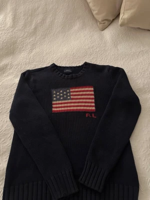 Ralph Lauren USA flagga tröja - Säljer en riktigt schysst och populär stickad tröja från Ralph Lauren. Tröjan är mörkblå och är väldigt tjock och varm vilket passar bra nu till vintern. Storleken är 14-16 vilket är ungefär Xs i vuxenstorlek och passar dig mellan 160-170 cm. Skicket är 9/10 då den knappast är använd. Skriv vid ytterligare frågor!✌️